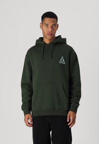 Sudadera de color verde oscuro hecha de una mezcla de algodón, con un bolsillo canguro, capucha con cordón y un logo triangular blanco en el pecho.