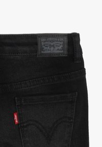 Jeans de mezclilla negra con un parche de cuero con "Levi Strauss & Co." y acento de etiqueta roja en el bolsillo trasero.