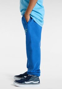 Blauwe joggingbroek met zijzakken, elastische boorden en een grafisch detail. Gecombineerd met marineblauwe sneakers met een logo-patroon.