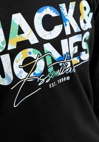 Fekete anyag, nagy fehér, kék, zöld és sárga fröccsentett felirattal: "Jack & Jones Essentials Est. 1990", aláírás-szerű vonallal.