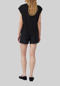 Zwarte top met kapmouwen gecombineerd met zwarte shorts, beide gemaakt van zachte stof. Zwarte instap schoenen maken de outfit compleet. Eenvoudig, minimalistisch ontwerp.