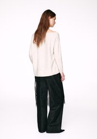 Cream knitted sweater paired with black wide-leg lace-trimmed trousers. The sweater features a relaxed fit and an off-shoulder neckline.