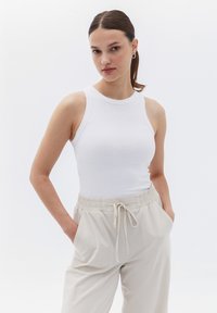 Weißes geripptes Tanktop mit rundem Ausschnitt, kombiniert mit beigen Hosen mit elastischem Bund und seitlichen Taschen.