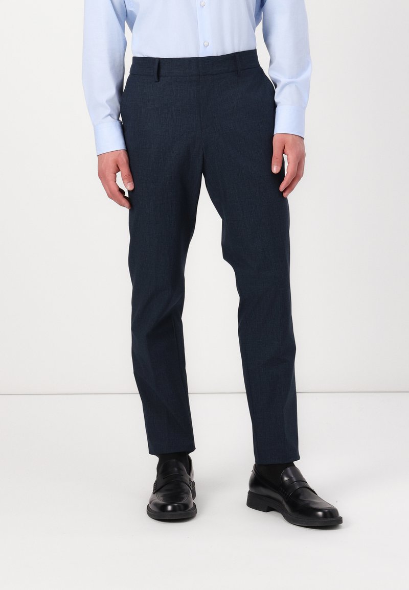 Navy blue trousers with a textured finish, slim fit design, belt loops, and front pockets, paired with black leather shoes.