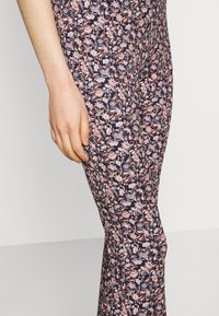 Blommönstrade leggings i marinblått med rosa och vita blommor. Tight passform, mjuk tygkvalitet och en synlig hand som vilar nära sidan.