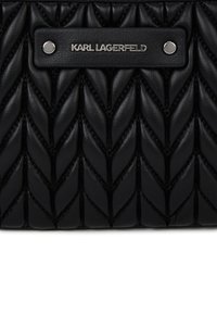 Mustmust kootud nahk, millel on kiirusõmblus ja ristkülikukujuline must nahk silt, kinnitatud kahe hõbedase nupuga, millel on tekst "KARL LAGERFELD".
