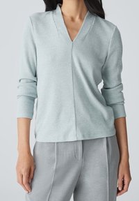 Ljusblå ribbad tröja med V-ringning och långa ärmar, matchad med gråbyxor. Tillverkad av mjukt material och har en avslappnad passform.