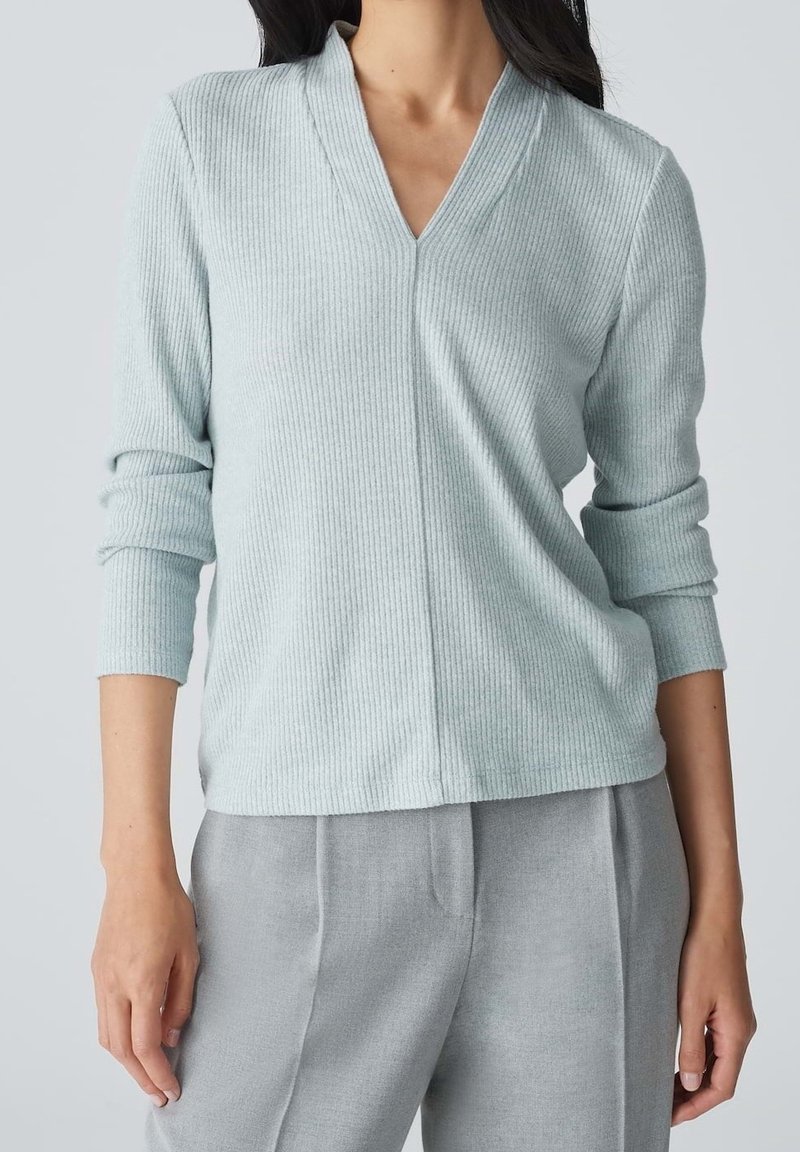 Ljusblå ribbad tröja med V-ringning och långa ärmar, matchad med gråbyxor. Tillverkad av mjukt material och har en avslappnad passform.