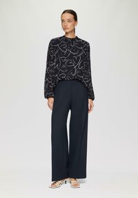 Blusa nera con motivo a cuore disegnato a mano bianco, maniche lunghe, abbinata a pantaloni ampi blu navy. Sandali con tacco bianchi e con cinturini completano il look.
