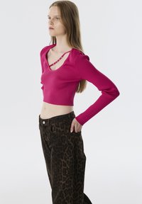 Top rose ajusté à côtes avec des manches longues, doté d'un décolleté en V et de détails décoratifs en lanières. Assorti à un jean à imprimé léopard sombre.