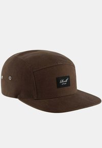 Gorra de algodón marrón con visera plana y una etiqueta negra en la parte frontal. Presenta ojales metálicos en los lados para ventilación.