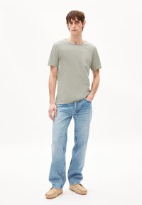 Hellgrünes Baumwoll-T-Shirt mit Rundhalsausschnitt. Hellblaue gerade Jeans. Braune Schuhe mit weicher Textur. Einfaches, lässiges Outfit.