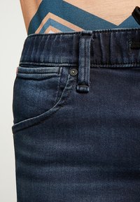 Mörka denimjeans med en klassisk femficksdesign, en åtsittande midja med bälteshällor och subtila sömnadsdetaljer på fickorna.