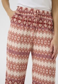 Pantalons légers et à motifs avec une coupe ample. Dotés d'un imprimé géométrique rouge et beige, d'une taille élastique et de poches latérales.
