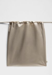 Beige tyggardin med samlad topp, slät textur, rektangulär form, lättviktig, har en sidolapp och subtil lyster.