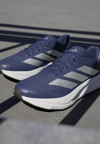 Scarpe sportive in mesh blu scuro con strisce argentate, caratterizzate da un collare imbottito, una superficie testurizzata e una suola bianca per la stabilità.