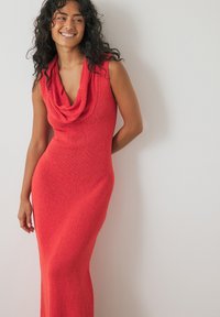 Punane, ilma varrukat mohäerõivastus kootud kleit, millel on kaela ümber käiv lõige. Ilusa fitt nihke ja pika hemiga. Tekstuuriga kangas lisab visuaalset huvi.