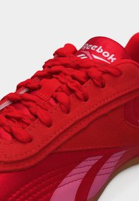 Φωτεινό κόκκινο αθλητικό παπούτσι Reebok με υφασμένα κορδόνια, επάνω μέρος από σουέτ και ροζ λεπτομέρεια λογότυπου στο πλάι και στη γλώσσα.