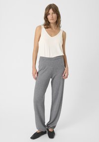 Helles cremefarbenes ärmelloses Top mit V-Ausschnitt, kombiniert mit lockeren, melierten grauen Hosen. Stricktextur und schlichtes Design. Schwarze, weiche Schuhe.