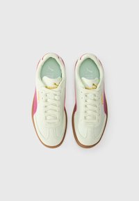 Baltās kedas ar rozā sānu svītru, zeltītu zīmolu un gumijas zolēm. Gluda tekstūra ar apaļu purngalu un auklu aizdari.