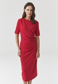 Punainen midi-mekko, joka on valmistettu sileästä kankaasta. Mekossa on lyhyet hihat, laskostettu muotoilu sivurypytyksellä ja venepääntie.
