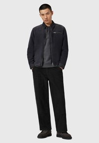 Giubbotto leggero di un blu navy scuro con colletto rialzato e tasca sul petto con zip, abbinato a pantaloni in velluto a coste neri e stivali texturizzati.