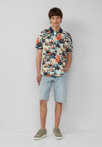 Polo manches courtes en bleu clair avec imprimé floral tropical et palmiers. Assorti à un short en denim clair et des baskets vertes.