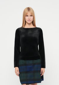 Top cu mâneci lungi din catifea neagră, cu un decolteu larg, asortat cu o fustă verde și albastră în carouri, având tiv drept și țesătură texturată.