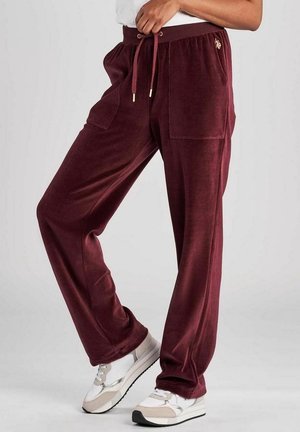 Pantalon large en velours couleur marron rouge avec poches plaquées et taille à cordon, porté avec des baskets blanches sur une personne debout.