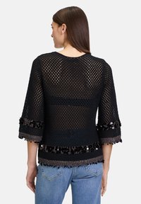 Schwarzes Häkeloberteil mit Dreiviertelärmel, das ein strukturiertes Design und Paillettenakzente am Saum aufweist. Leicht und halbtransparent.
