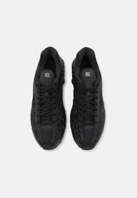 Paire de baskets Nike Shox noires avec semelles texturées et lacets, vues de dessus sur fond blanc.