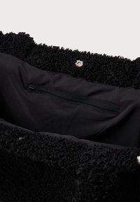 Zwarte tas met een gestructureerd, fluffy buitenmateriaal en een gladde binnenvoering. Beschikt over een klein ritsvak en een drukknoopsluiting.