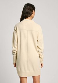 Abito lavorato a maglia beige con colletto alto, maniche lunghe, polsini a coste e taglio dritto. Presenta un discreto motivo a righe lungo la schiena.