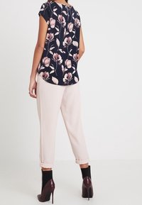 Blusa a maniche corte navy a fiori con motivi di fiori rosa e crema; abbinata a pantaloni rosa chiaro con risvolto e tacchi scuri.