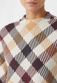 Strickpullover mit einem geometrischen Diamantmuster in warmen Farben (Orange, Burgundy, Schwarz) und strukturierten Streifen auf einem cremefarbenen Hintergrund.