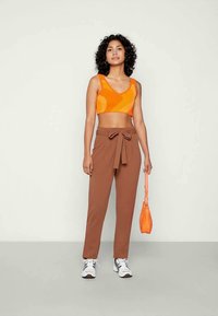 Top cropped com padrão laranja, calças de cintura alta castanhas com um laço na cintura, e uma pequena bolsa laranja. Ténis brancos completam o visual.