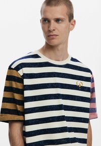 Striped cotton t-shirt featuring horizontal navy, cream, gold, and pink stripes, with a round neckline and a small logo on the chest.