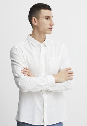 Camisa blanca de manga larga y botones, hecha de una tela ligera y texturizada. Presenta un bolsillo en el pecho y puños abotonados.