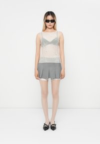 Top trasparente con ricami floreali, mini gonna plissettata grigia, rifiniture in pizzo, calze leggere e scarpe con tacco nere. Gli occhiali da sole circolari completano il look.