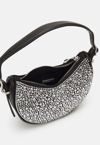 Bolso negro de forma curva, adornado con tachuelas plateadas, con cierre de cremallera y una correa corta. Exterior suave, diseño minimalista.