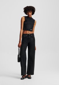 Top scurt din denim negru cu guler înalt; asortat cu blugi negri din denim cu picioare largi, accesorizat cu o mică geantă de umăr neagră și pantofi cu studuri.