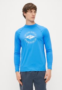 Μπλε rash guard με μακριά μανίκια, κωδικό στρογγυλής λαιμόκοψης, κεντρικό λογότυπο με κείμενο και επίπεδες ραφές για άνεση. Ελαφρύ και ελαστικό ύφασμα.