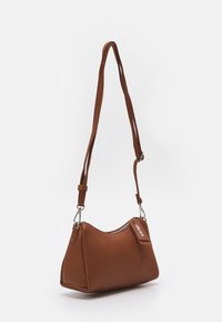 Malá hnědá kožená taška na rameno s nastavitelným popruhem a zipovým uzávěrem, umístěná na jednobarevném bílém pozadí.