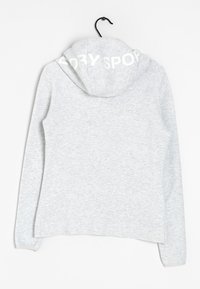 Ljusgrå luvtröja med texten "DRY SPORT" på baksidan av luvan, upphängd på en svart galge mot en vit bakgrund.