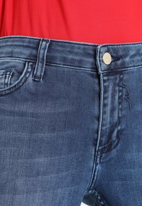 Jeans in denim con un lavaggio blu medio, design a cinque tasche, chiusura con bottone dorato e dettagli di cucitura discreti sulla tasca frontale.