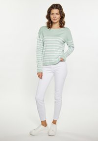 Maglione verde chiaro con righe orizzontali bianche, abbinato a jeans skinny bianchi e sneakers bianche. Il maglione presenta una vestibilità comoda e maniche lunghe.
