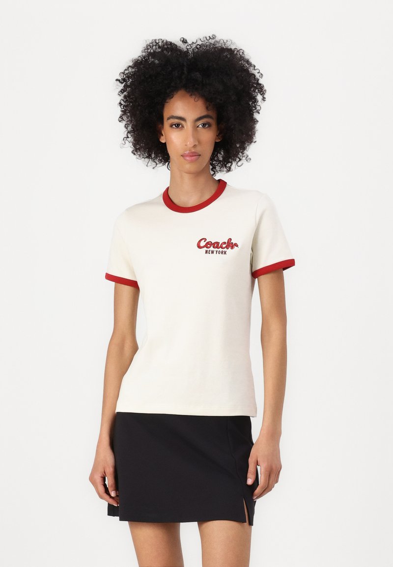Witte katoenen T-shirt met rode ribbelkraag en mouwen, met "Coach New York" in het rood geborduurd op de linkerborst.