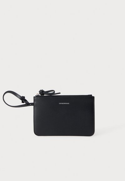 Pochette noire Emporio Armani avec fermeture éclair et bracelet poignet sur fond clair.