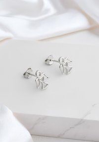 Orecchini a forma di angelo astratto con ali in argento, caratterizzati da un piccolo cuore al centro. Finitura liscia, design minimalista.