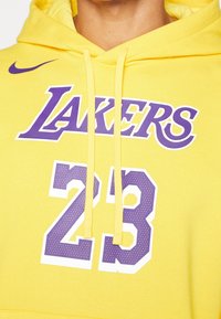 Sweat à capuche jaune avec logo violet des Lakers et numéro 23, avec cordons et un swoosh Nike sur la poitrine.